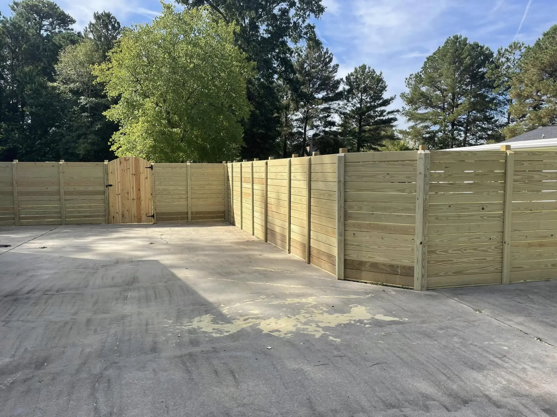Horizontal privacy fence enclosure with an arched wooden gate around a concrete drive