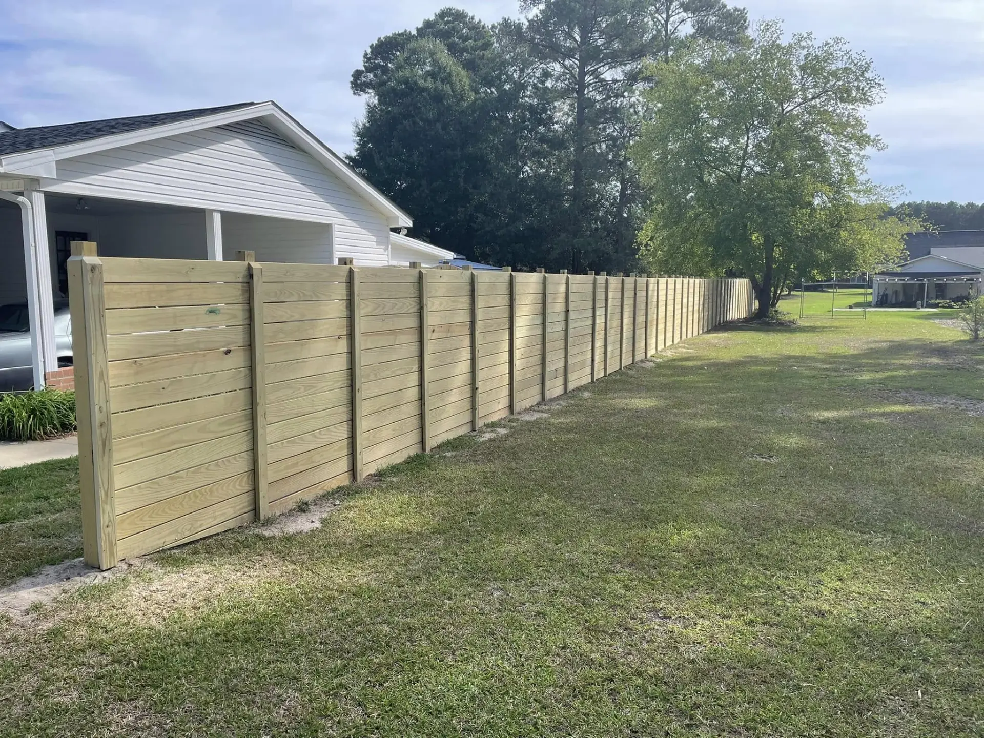 New horizontal-board pressure-treated privacy fence running along a residential property line