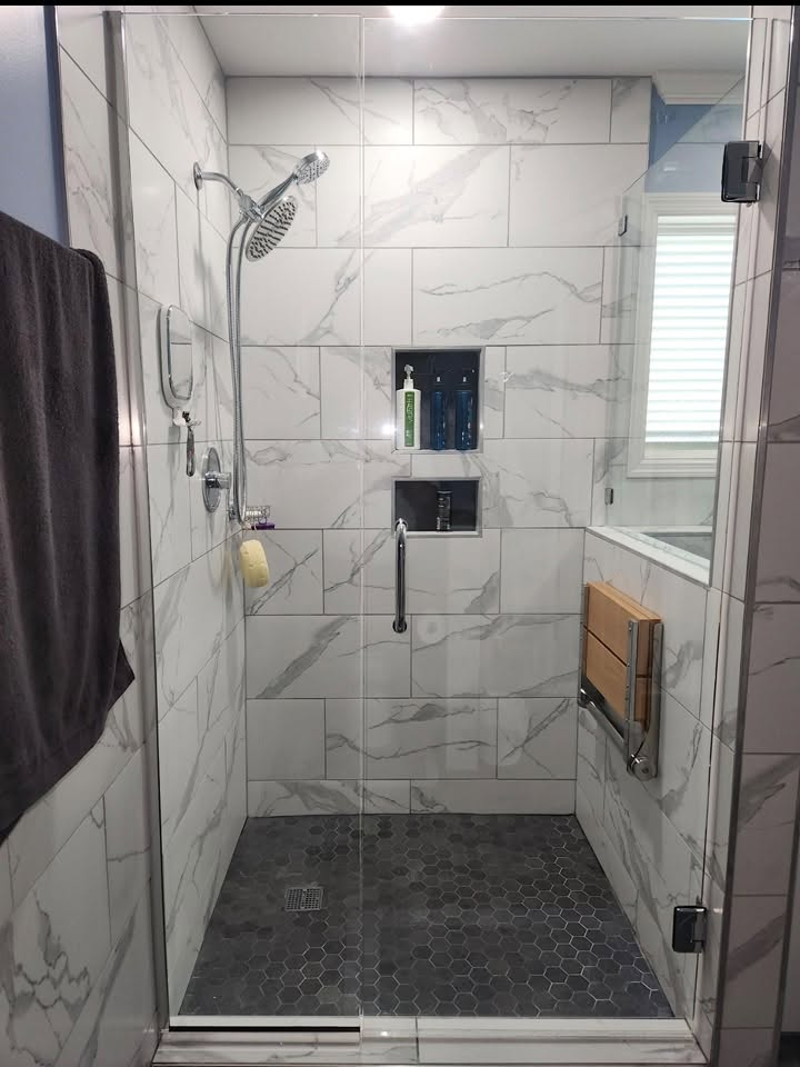 Walk-in shower with marble-look tile, glass enclosure, and built-in niches