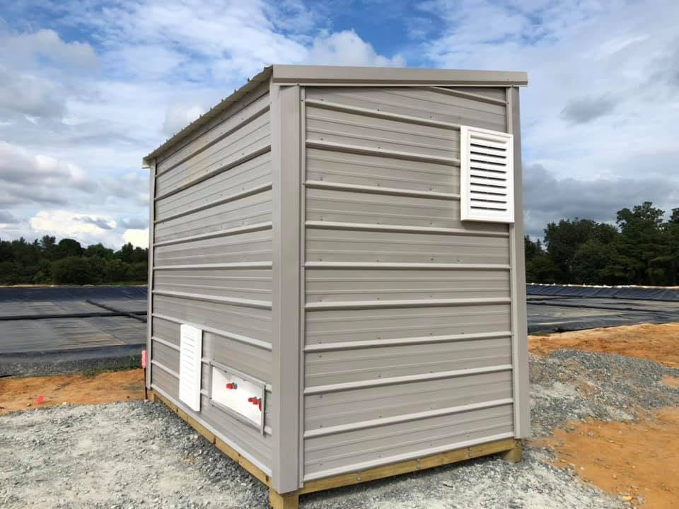 New metal-sided utility building with louvered vents on a gravel pad